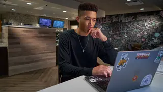 A student sits at a table at The Perk and is looking at a laptop screen