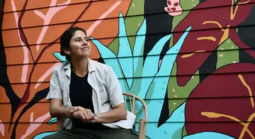 Zadith Rodriguez sits in front of a brightly colored mural