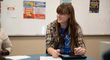 Natasha sits a table in the Language Lab. She is conversing with other people out of frame.