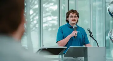 Luke Crocker stands at a podium and speaks into a microphone at a reception honoring his accomplishment