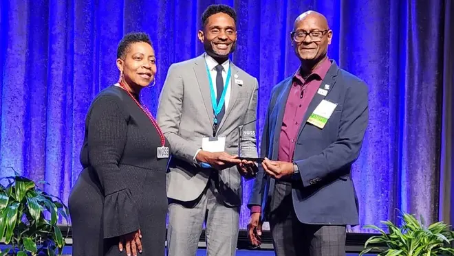 A woman presents the NOSS Award to Douglas Allen and Dewayne Dickens.