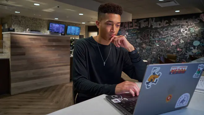 A student sits at a table at The Perk and is looking at a laptop screen