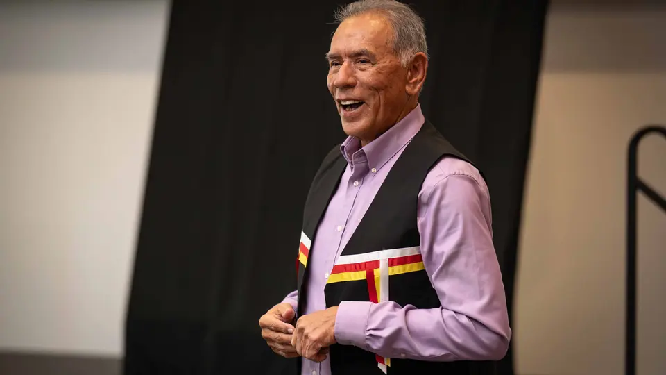 Wes Studi stands on a stage and is smiling.