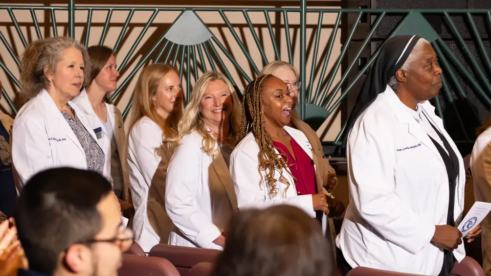 Faculty in white coats are standing and smiling at the ceremony.