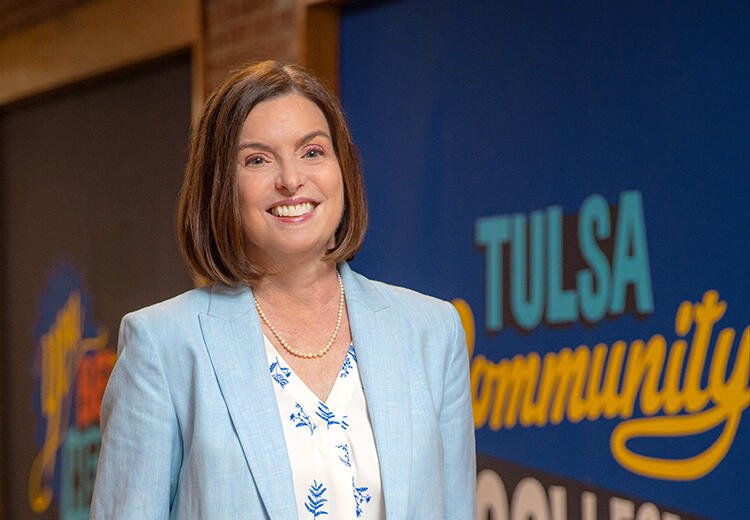 TCC president Leah Goodson smiles, wearing a light blue suit jacket and floral shirt..