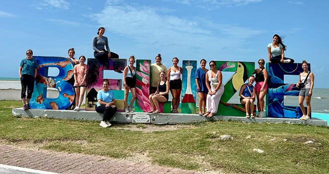 TCC early childhood students stand next to a sign spelling the word "Belize"