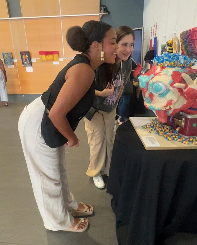 Two women admire a sculpture featuring wrapped piece of bubble gum.